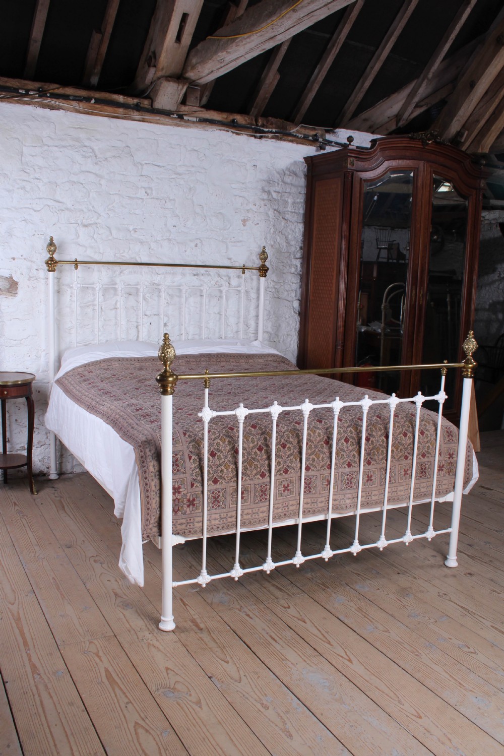 A Victorian white painted iron bedstead featuring brass top rails and brass urn finials on the headboard and footboard. View IX