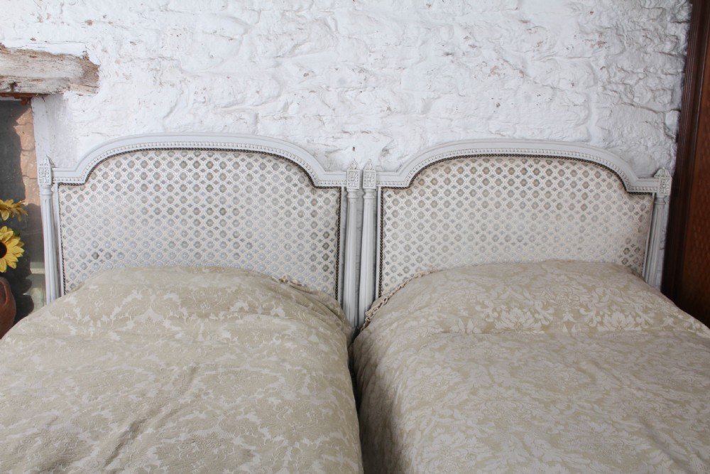 A pair of off-white painted French Empire style single bed frames featuring upholstered arched headboards and matching footboards with geometric fabric. View II