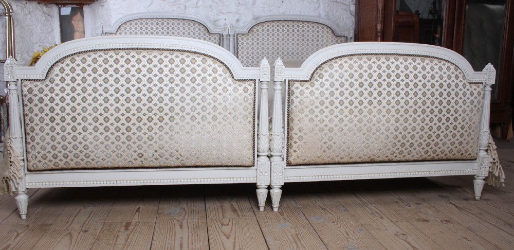 A pair of off-white painted French Empire style single bed frames featuring upholstered arched headboards and matching footboards with geometric fabric. View III