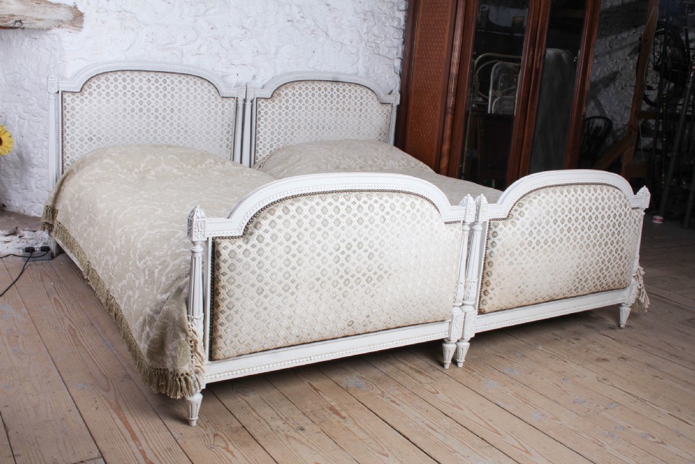 A pair of off-white painted French Empire style single bed frames featuring upholstered arched headboards and matching footboards with geometric fabric. View VI