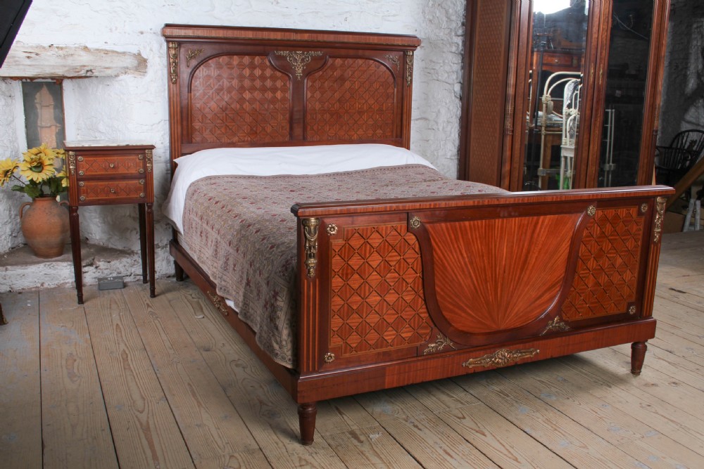 A French Empire style king size bed frame crafted from mahogany with diamond geometric fruitwood parquetry inlays and decorative brass mounts.