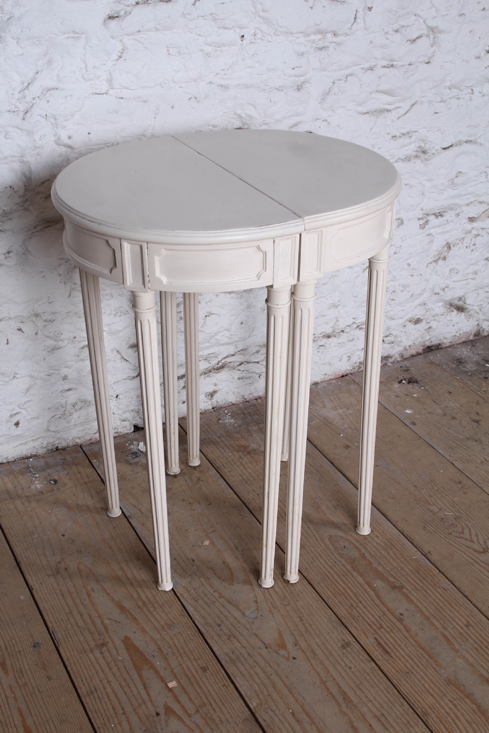A pair of off-white painted demi-lune console tables with panelled aprons and slender fluted turned legs. View III