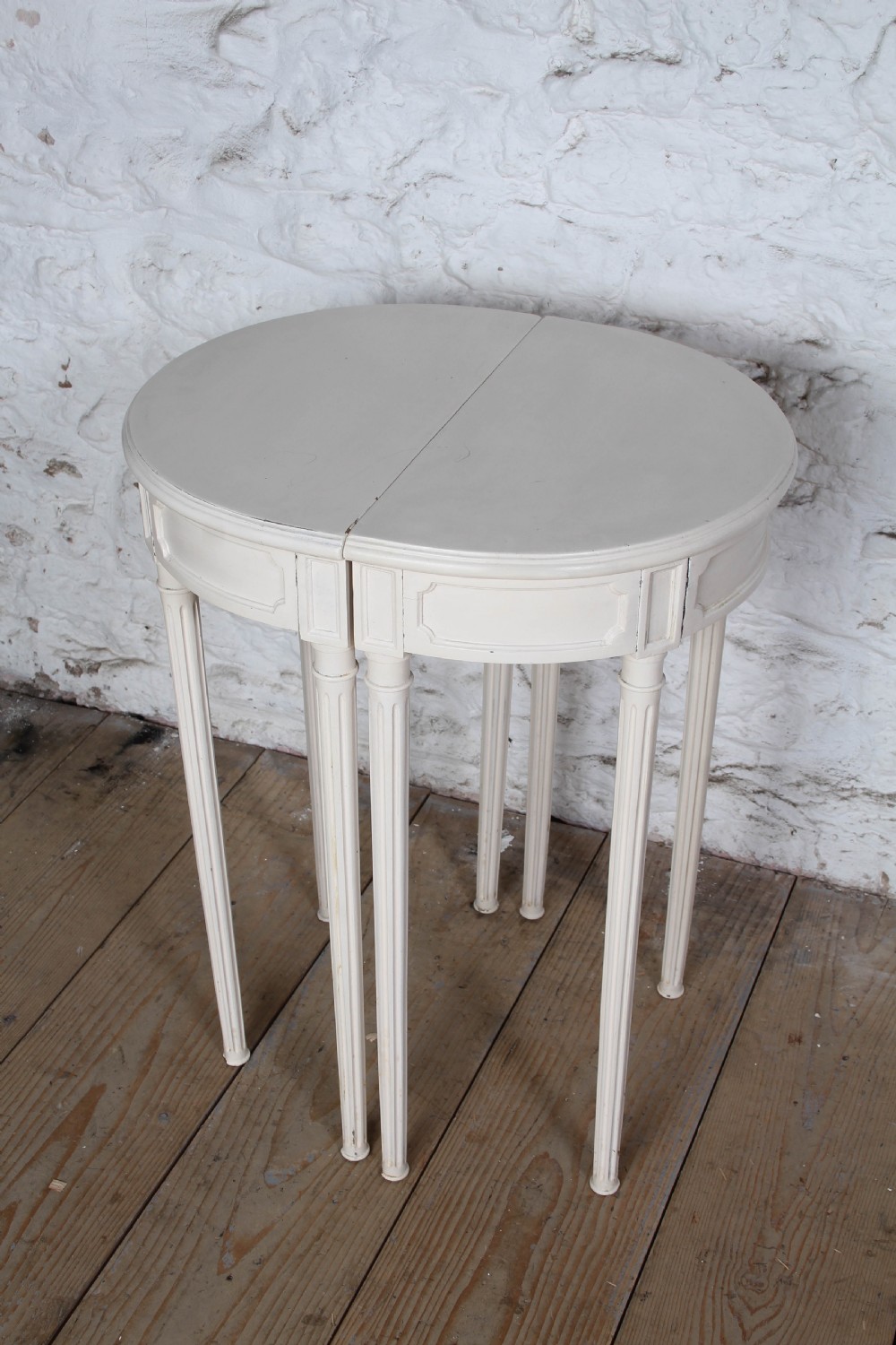 A pair of off-white painted demi-lune console tables with panelled aprons and slender fluted turned legs. View IV