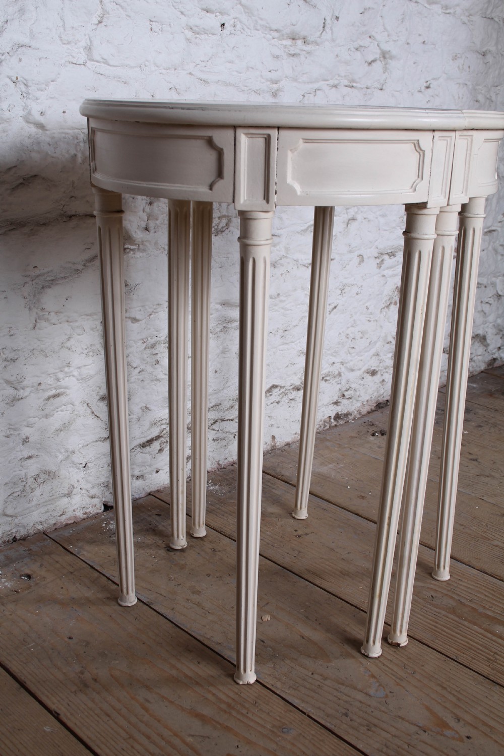 A pair of off-white painted demi-lune console tables with panelled aprons and slender fluted turned legs. View V