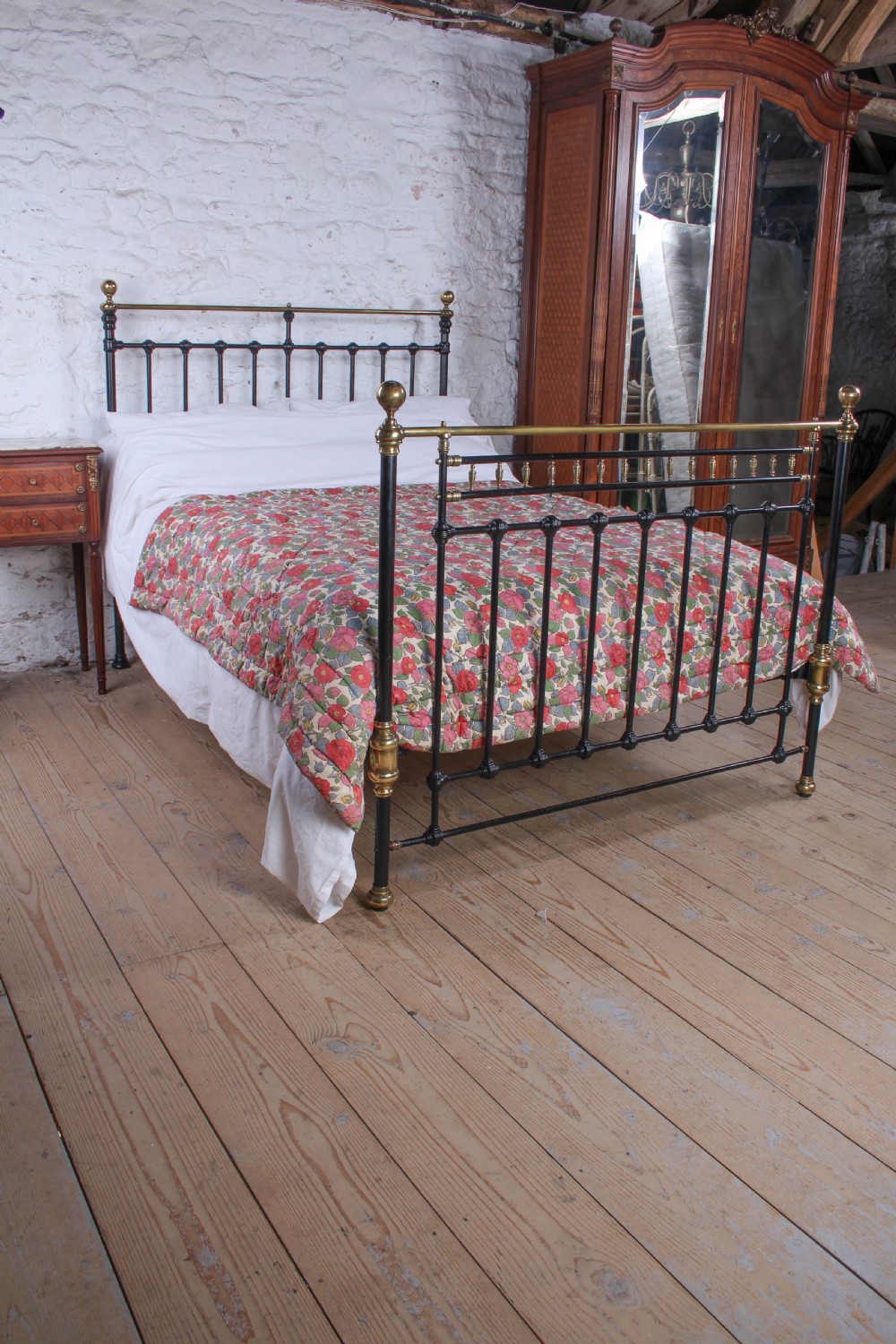 A Victorian double bedstead featuring a black painted cast iron frame, brass top rails, and spherical brass finials.