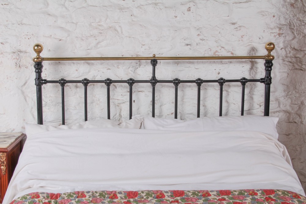 A Victorian double bedstead featuring a black painted cast iron frame, brass top rails, and spherical brass finials. View VII