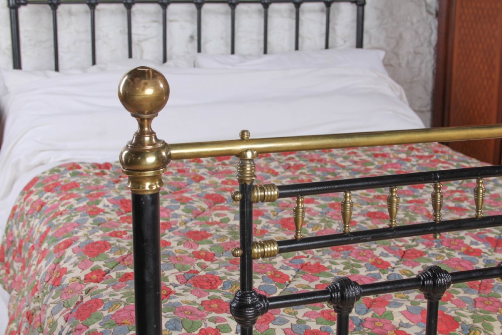 A Victorian double bedstead featuring a black painted cast iron frame, brass top rails, and spherical brass finials. View VIII