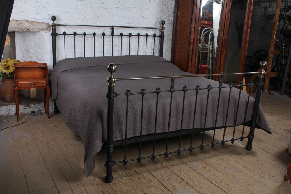 A super king size bedstead featuring a black iron frame with vertical spindles, cast rosettes, and brass top rails with brass ball finials. View II