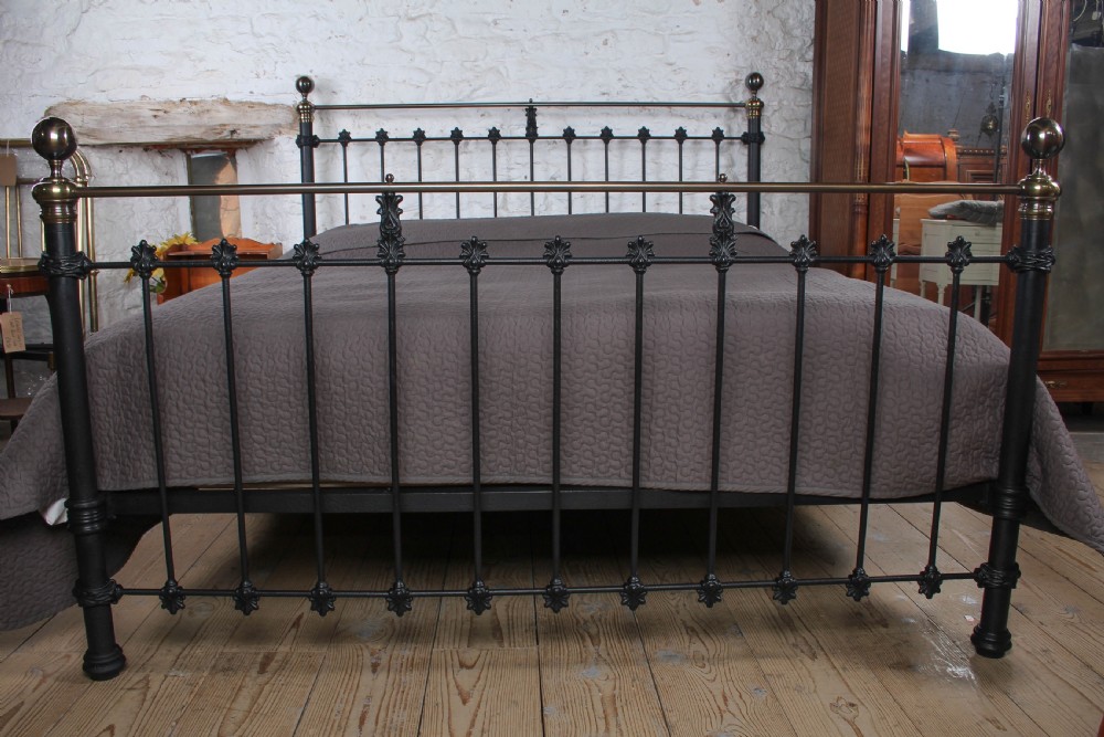 A super king size bedstead featuring a black iron frame with vertical spindles, cast rosettes, and brass top rails with brass ball finials. View V