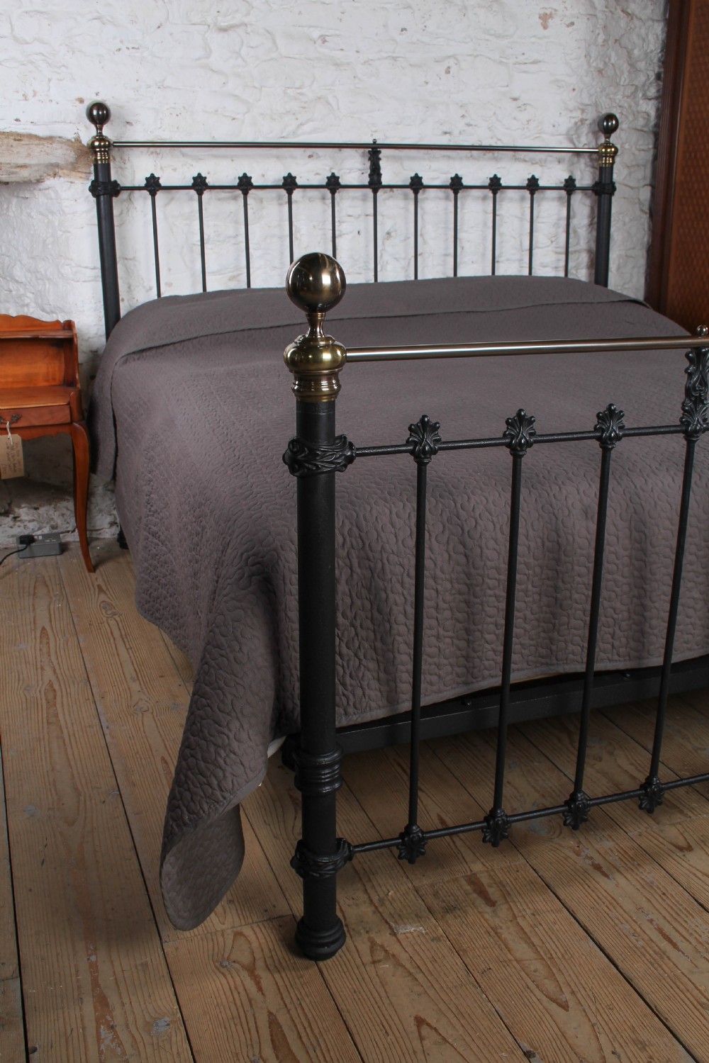 A super king size bedstead featuring a black iron frame with vertical spindles, cast rosettes, and brass top rails with brass ball finials. View VIII
