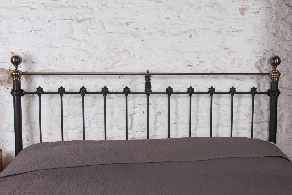 A super king size bedstead featuring a black iron frame with vertical spindles, cast rosettes, and brass top rails with brass ball finials. View IX