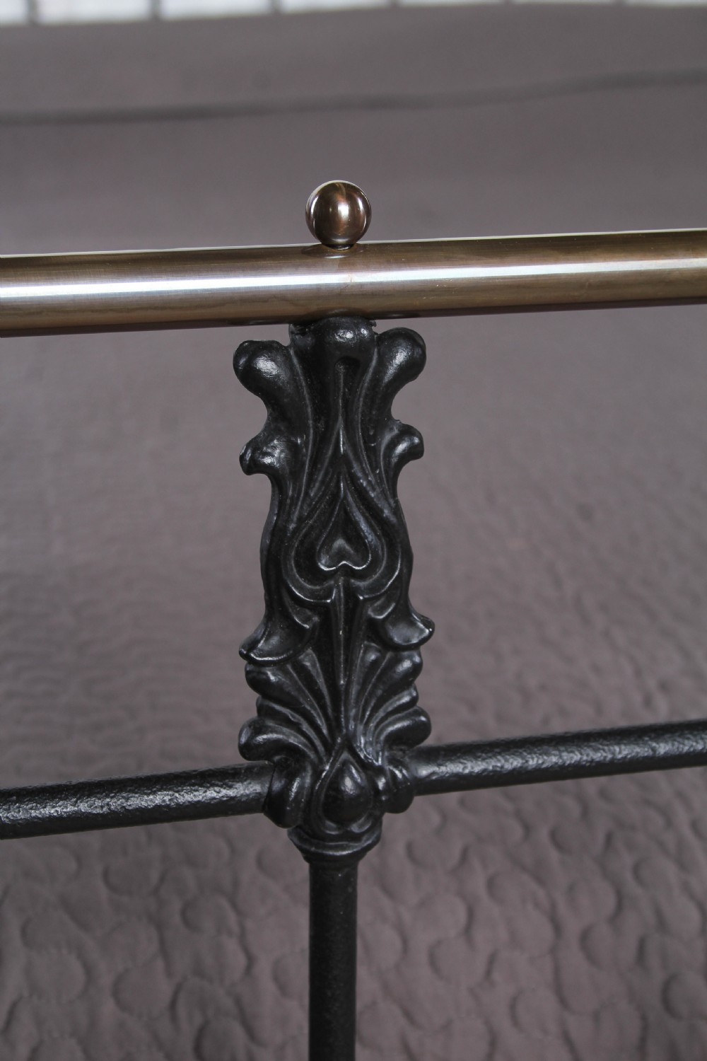 A super king size bedstead featuring a black iron frame with vertical spindles, cast rosettes, and brass top rails with brass ball finials. View X