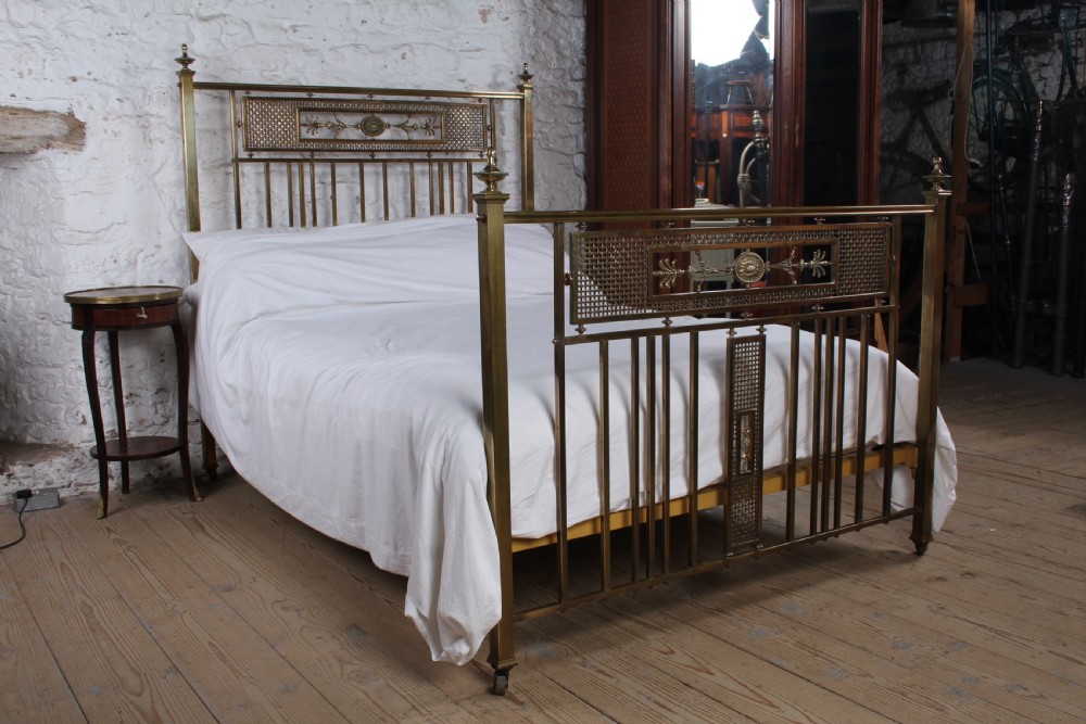 An antique French brass double bed frame with ornamental lattice headboard and footboard panels, vertical spindles, and finial corner posts.