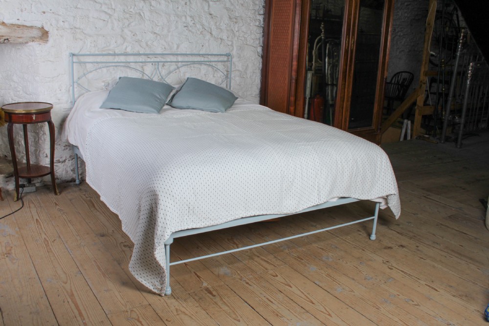 A light blue painted forged iron king-size bedstead featuring a simple arched headboard with decorative scrollwork.