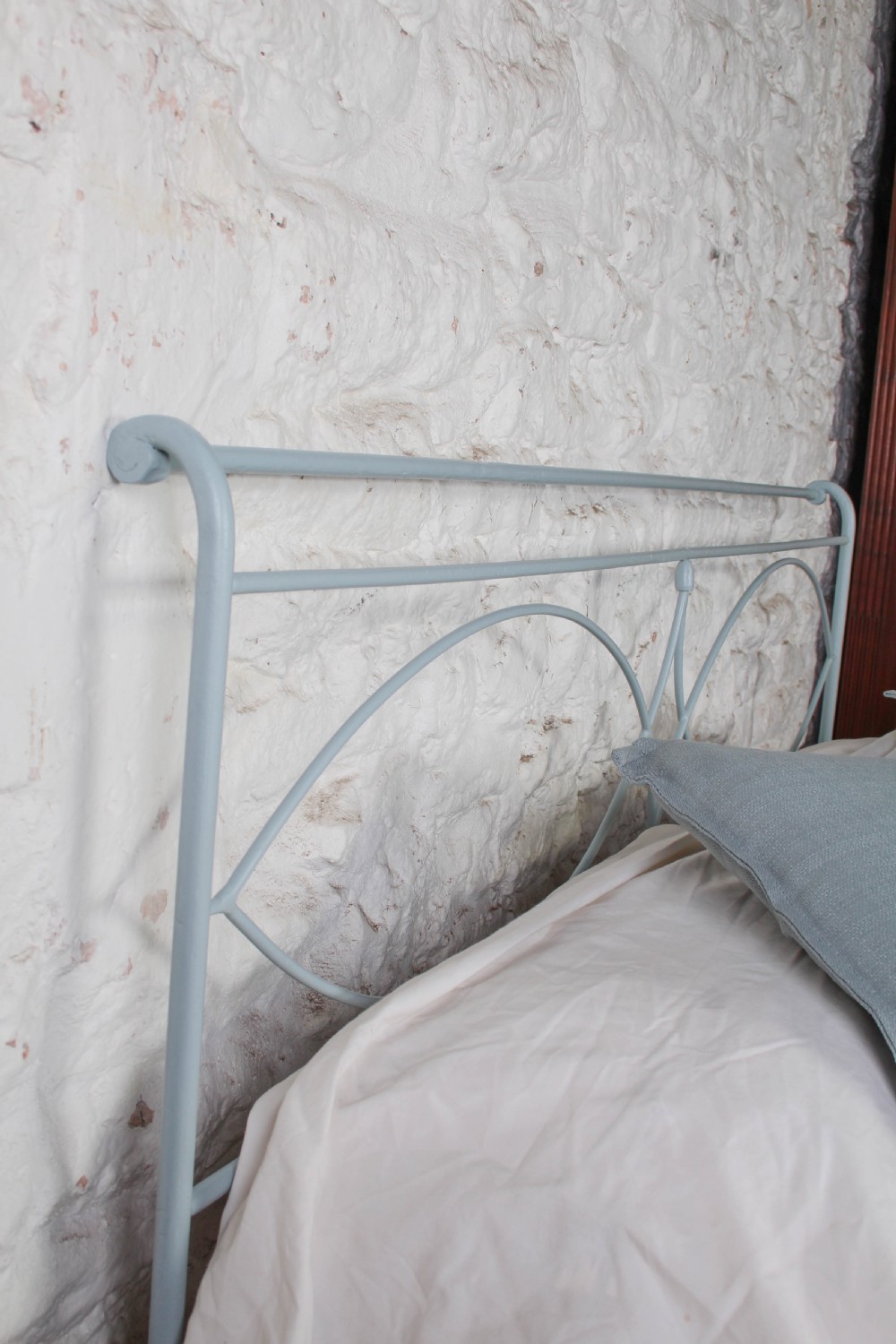 A light blue painted forged iron king-size bedstead featuring a simple arched headboard with decorative scrollwork. View V