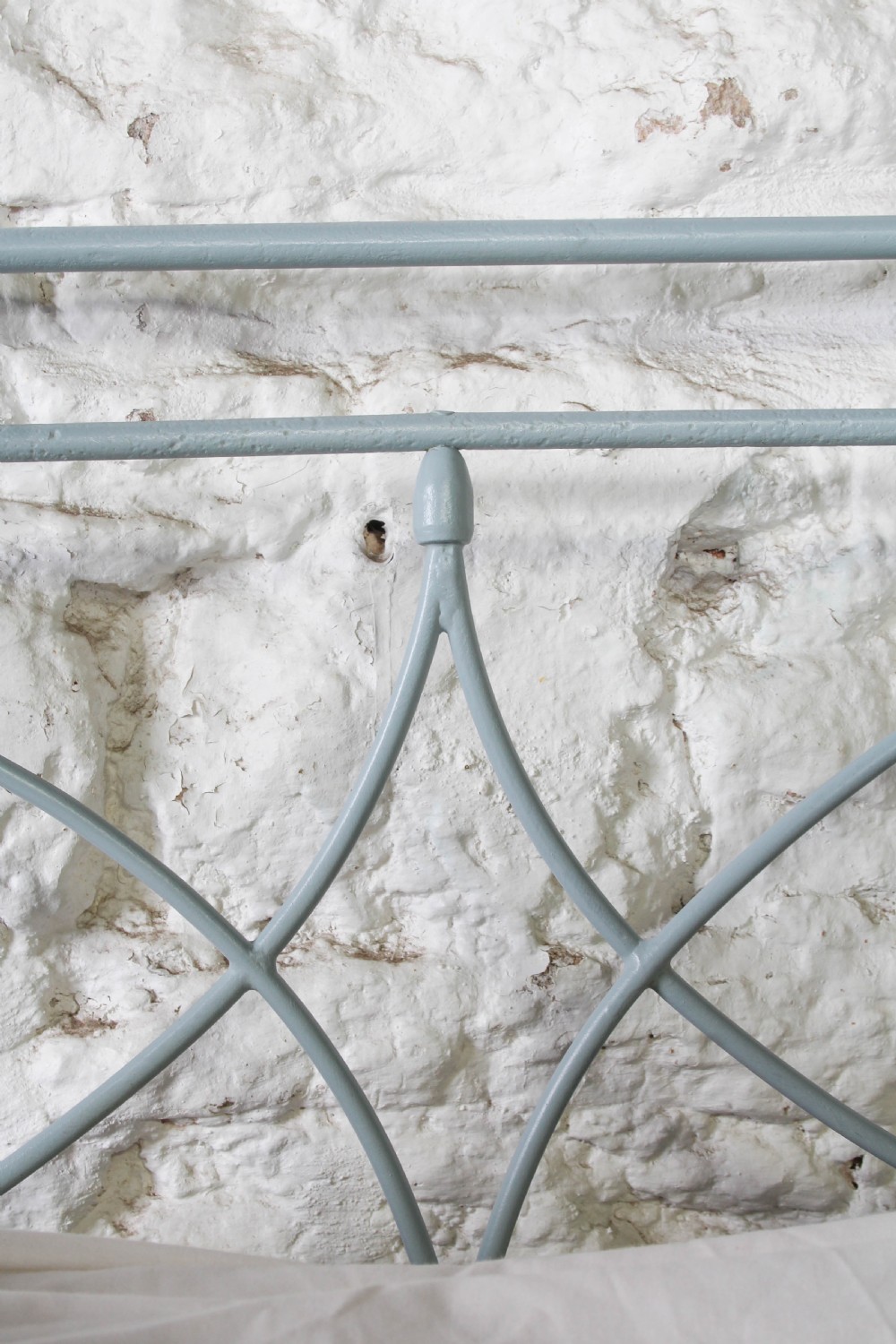 A light blue painted forged iron king-size bedstead featuring a simple arched headboard with decorative scrollwork. View VI