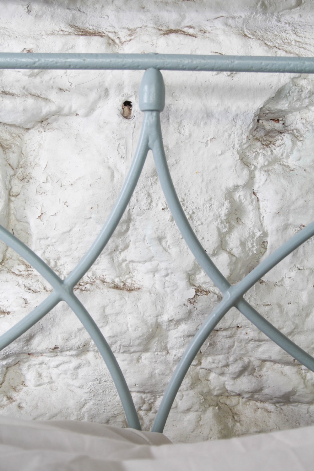 A light blue painted forged iron king-size bedstead featuring a simple arched headboard with decorative scrollwork. View VII