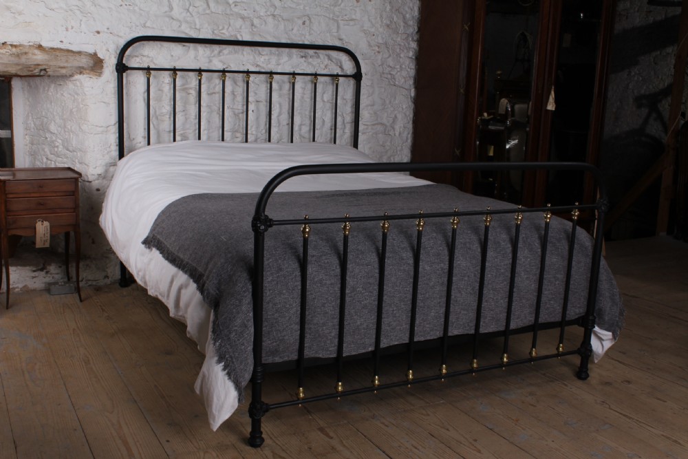 A king size black painted iron bedstead featuring rounded top rails, vertical tubular spindles, and decorative brass finials.