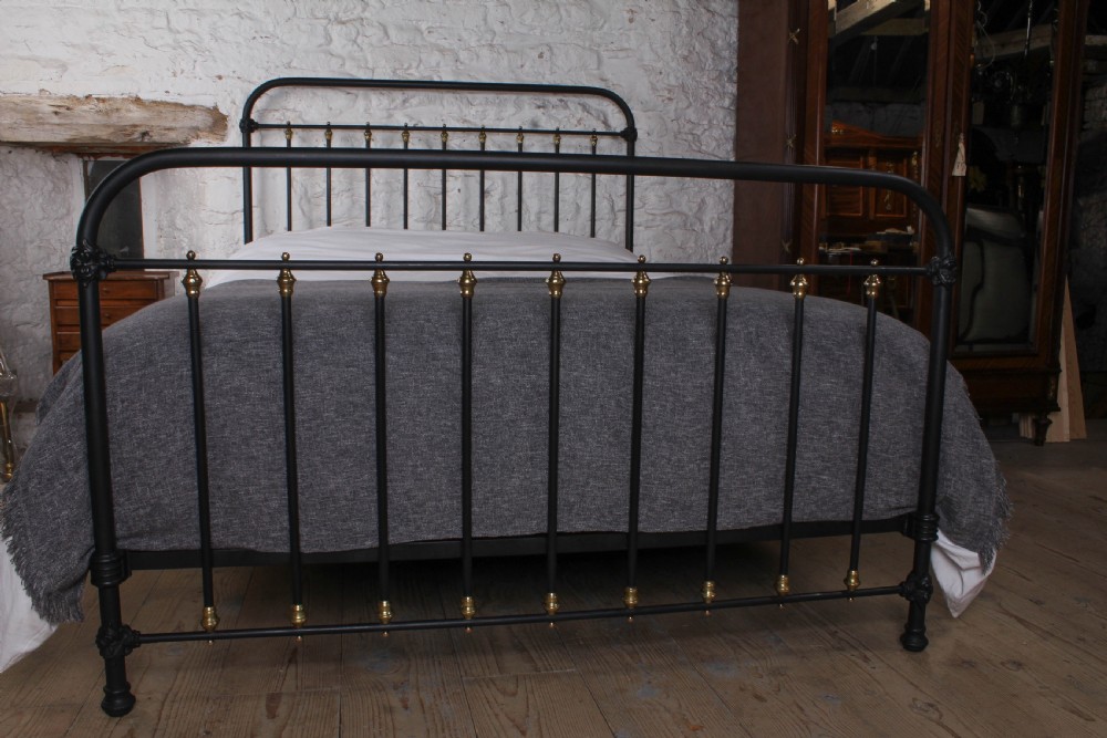 A king size black painted iron bedstead featuring rounded top rails, vertical tubular spindles, and decorative brass finials. View II