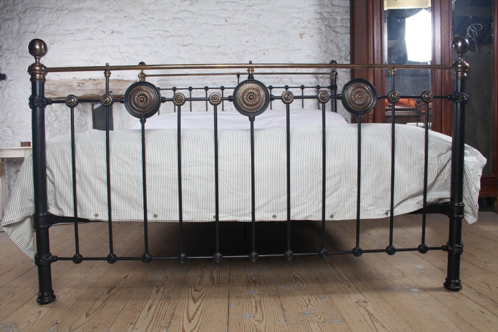 A Victorian black iron and brass super king-size bedstead featuring vertical spindles, circular brass medallions on the footboard, and brass top rails with spherical finials. View III