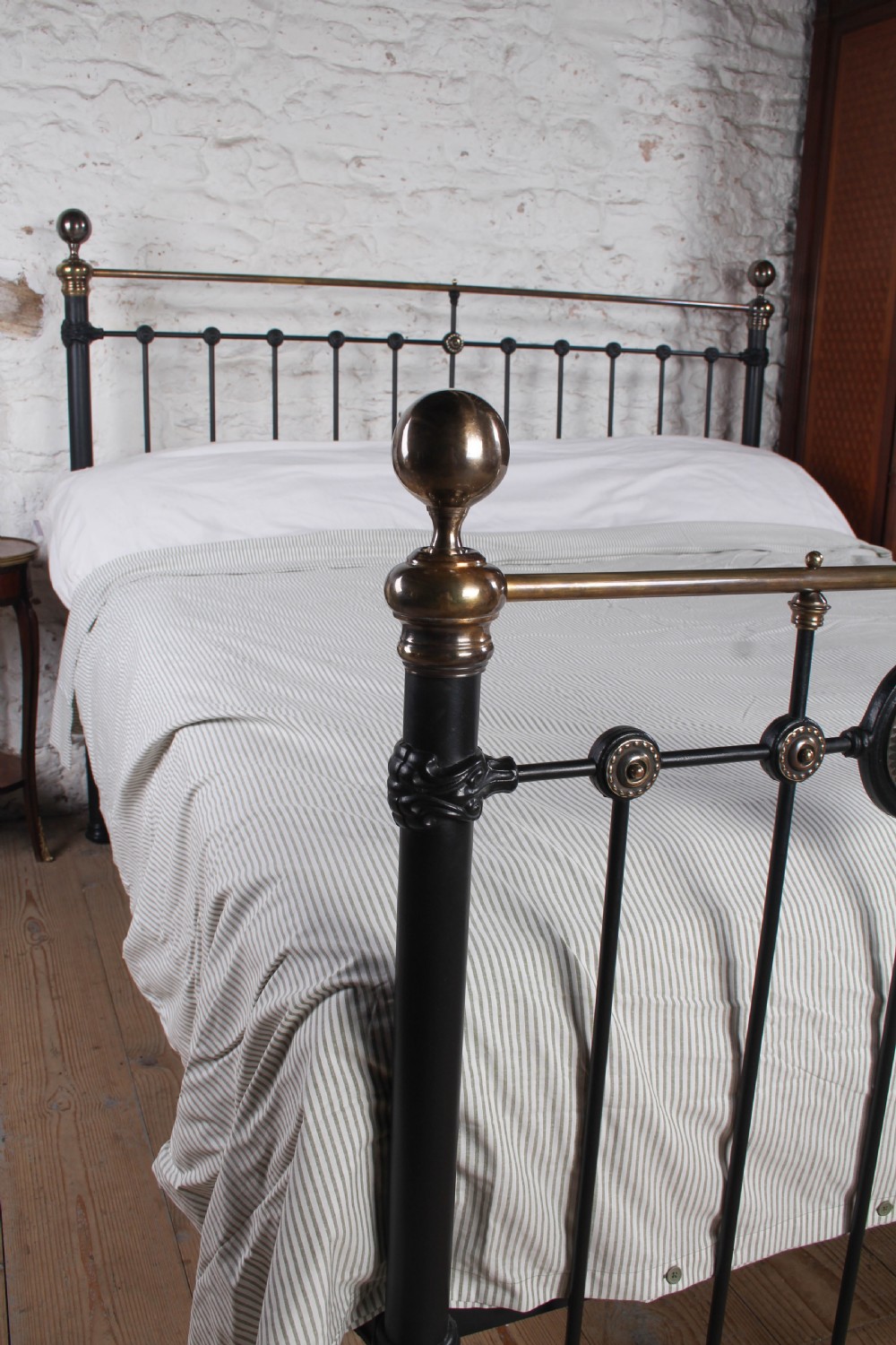 A Victorian black iron and brass super king-size bedstead featuring vertical spindles, circular brass medallions on the footboard, and brass top rails with spherical finials. View VI