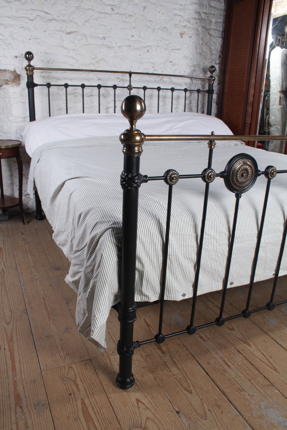 A Victorian black iron and brass super king-size bedstead featuring vertical spindles, circular brass medallions on the footboard, and brass top rails with spherical finials. View VII