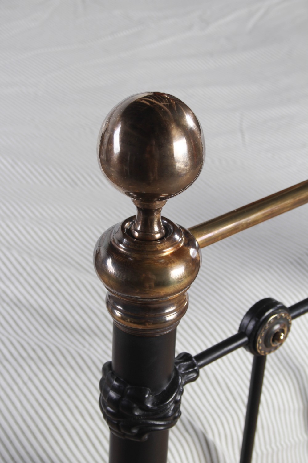 A Victorian black iron and brass super king-size bedstead featuring vertical spindles, circular brass medallions on the footboard, and brass top rails with spherical finials. View VIII