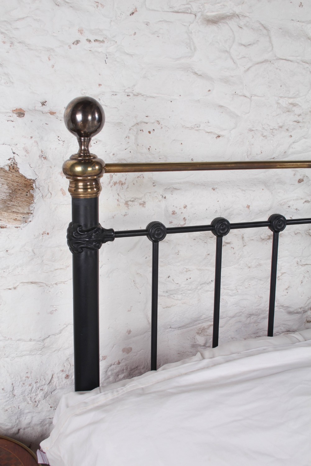 A Victorian black iron and brass super king-size bedstead featuring vertical spindles, circular brass medallions on the footboard, and brass top rails with spherical finials. View X