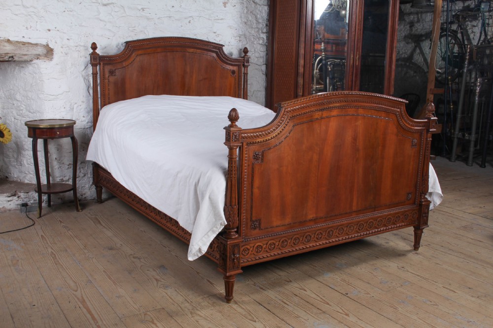 A carved walnut king-size bedstead featuring an arched headboard and footboard framed by fluted corner posts and decorative finials.
