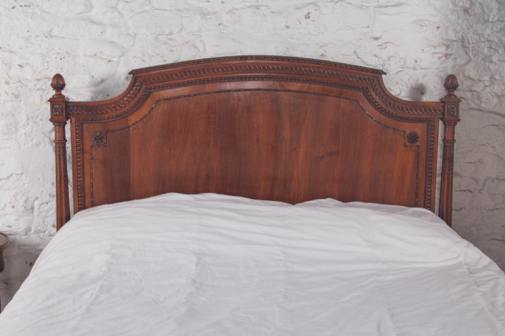 A carved walnut king-size bedstead featuring an arched headboard and footboard framed by fluted corner posts and decorative finials. View III