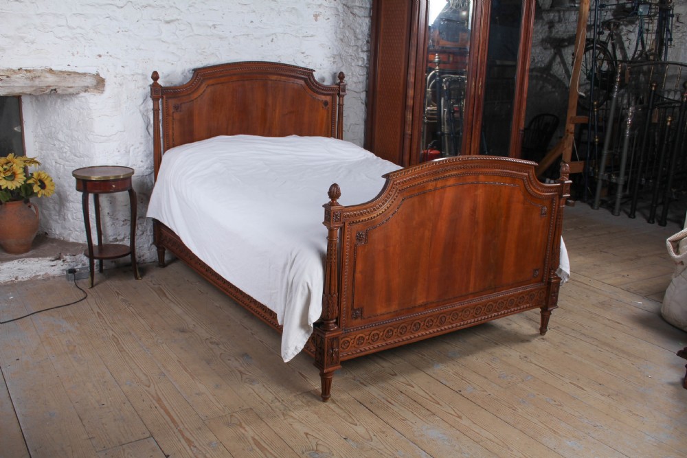 A carved walnut king-size bedstead featuring an arched headboard and footboard framed by fluted corner posts and decorative finials. View VIII