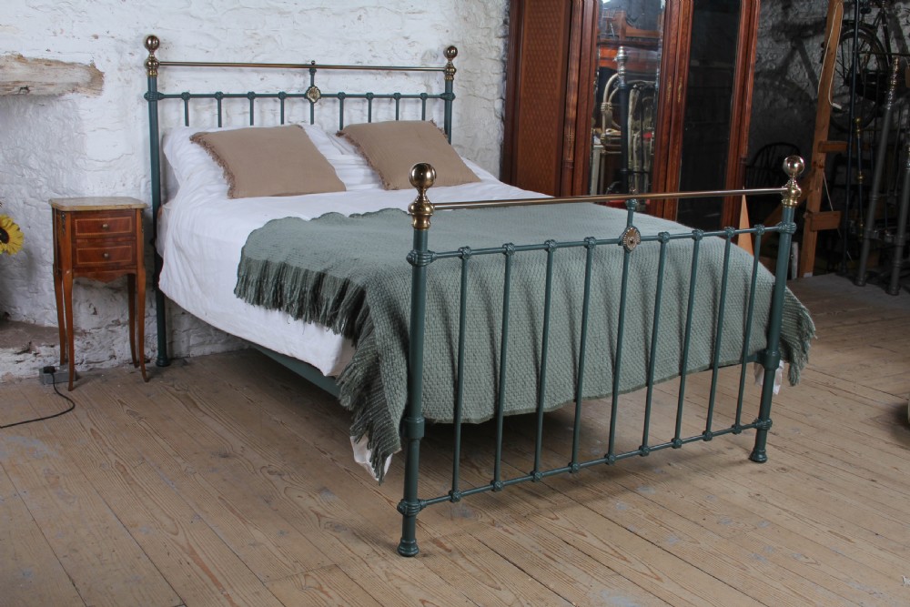 A Victorian metal bedstead featuring dark green painted iron uprights, vertical spindles, brass top rails, and brass finials.