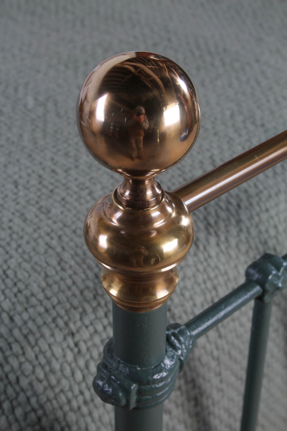 A Victorian metal bedstead featuring dark green painted iron uprights, vertical spindles, brass top rails, and brass finials. View II