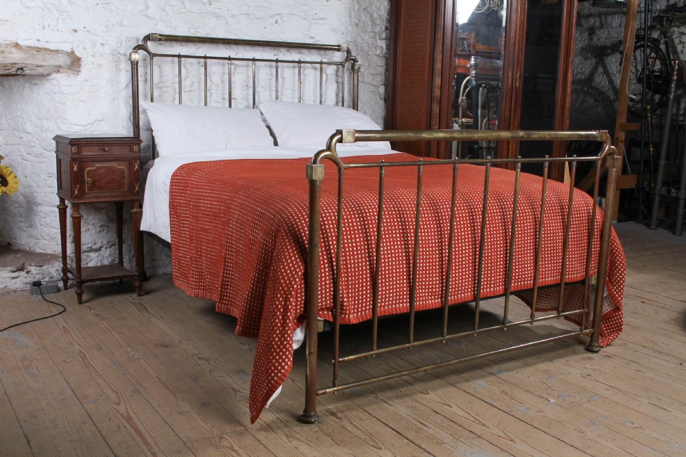 An antique brass king-size bedstead with vertical spindles, rounded tubular top rails, and cast iron corner connections.