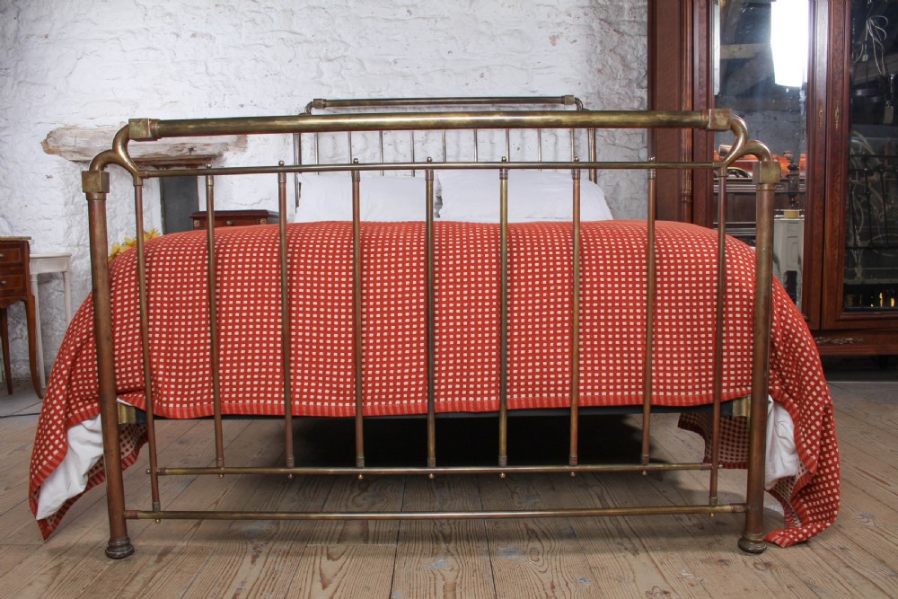 An antique brass king-size bedstead with vertical spindles, rounded tubular top rails, and cast iron corner connections. View III