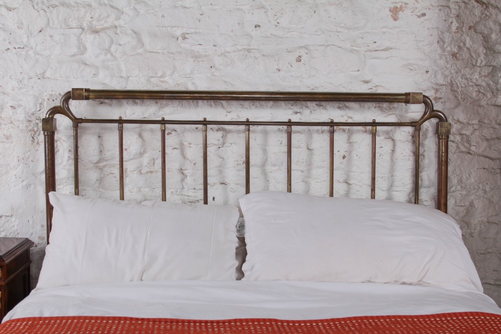 An antique brass king-size bedstead with vertical spindles, rounded tubular top rails, and cast iron corner connections. View VI