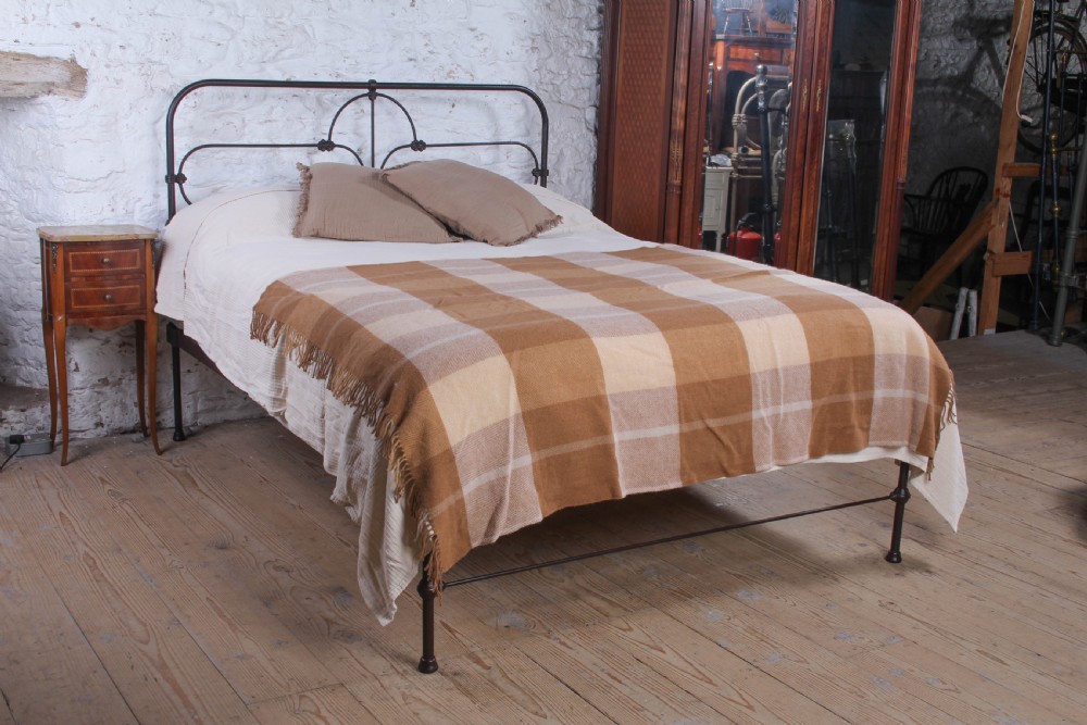 An antique dark iron king size bedstead featuring an arched headboard with decorative scrollwork and a low footrail design.