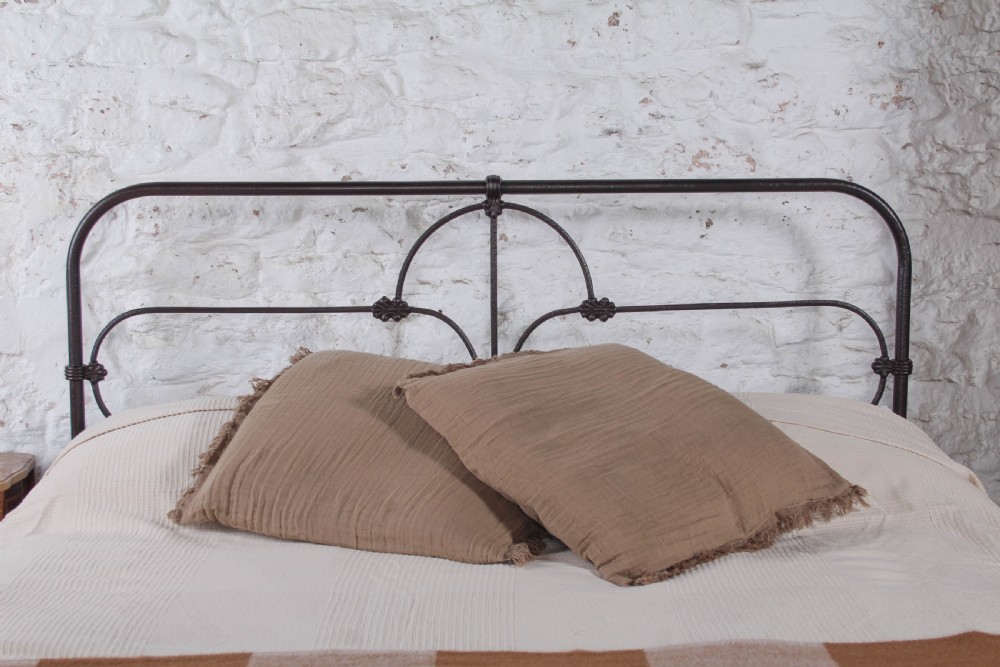 An antique dark iron king size bedstead featuring an arched headboard with decorative scrollwork and a low footrail design. View III