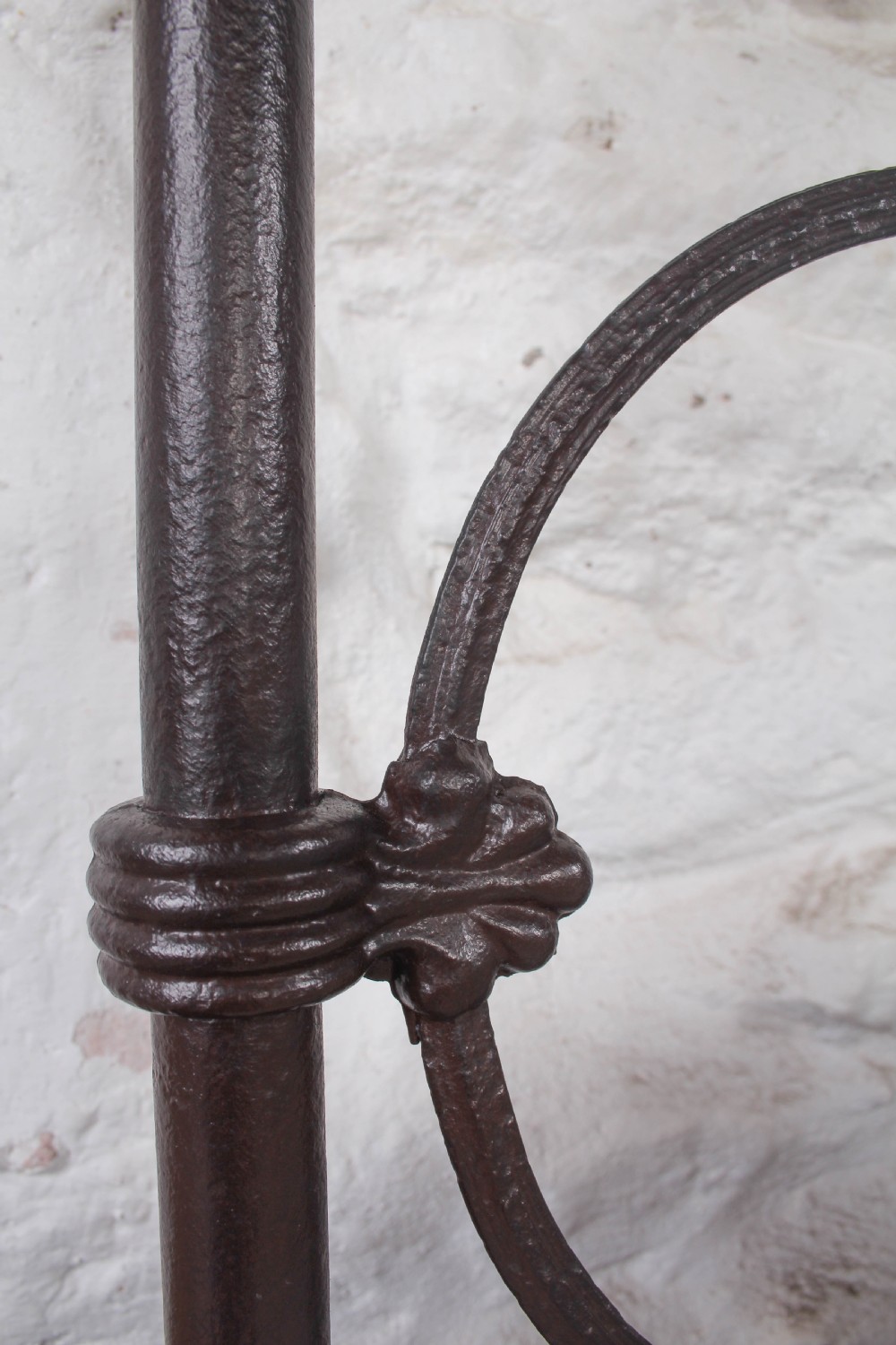 An antique dark iron king size bedstead featuring an arched headboard with decorative scrollwork and a low footrail design. View IV