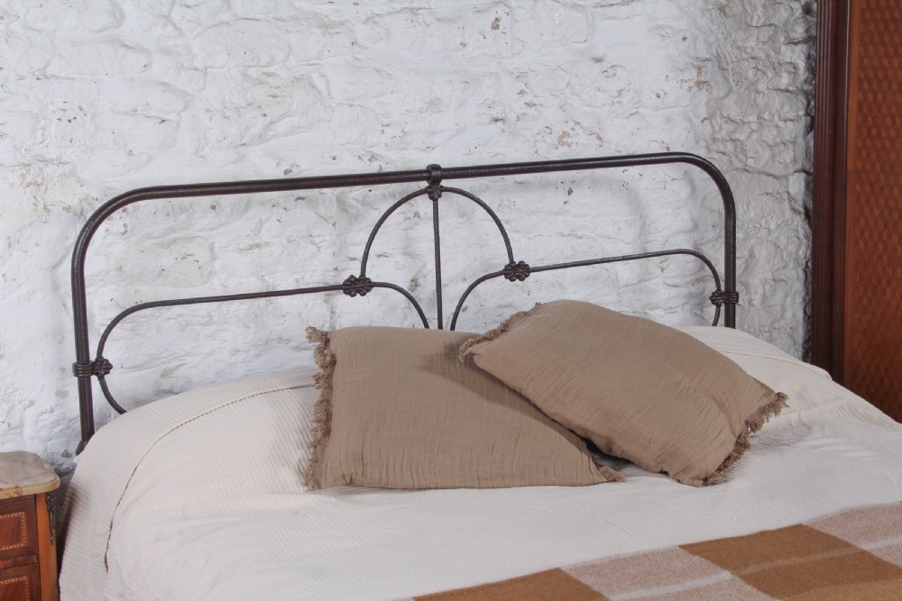 An antique dark iron king size bedstead featuring an arched headboard with decorative scrollwork and a low footrail design. View VI