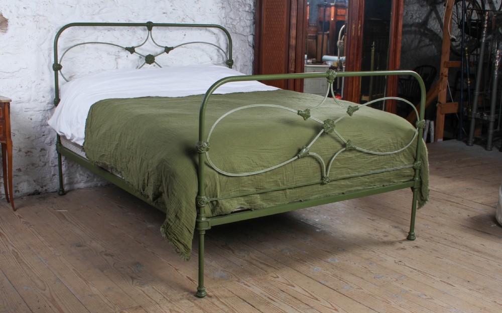 A green painted cast iron king-size bedstead featuring decorative central rosette castings, curved top rails, and metal strapwork.