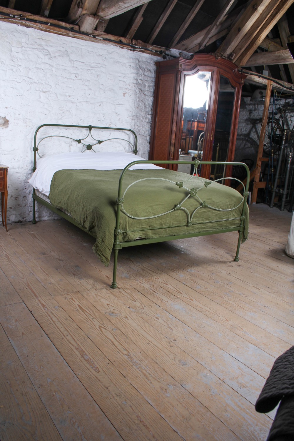 A green painted cast iron king-size bedstead featuring decorative central rosette castings, curved top rails, and metal strapwork. View II