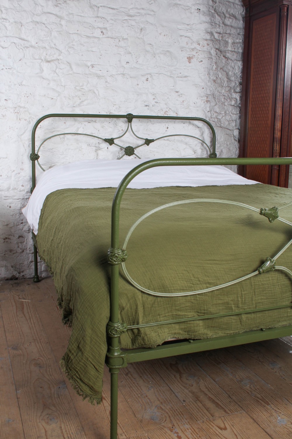 A green painted cast iron king-size bedstead featuring decorative central rosette castings, curved top rails, and metal strapwork. View III