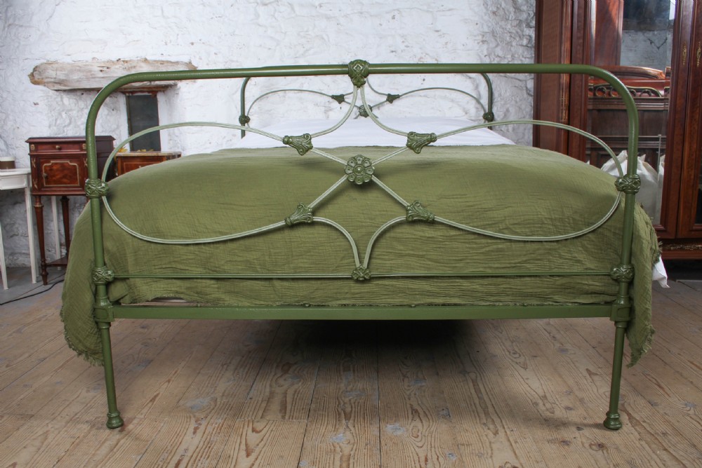 A green painted cast iron king-size bedstead featuring decorative central rosette castings, curved top rails, and metal strapwork. View IV