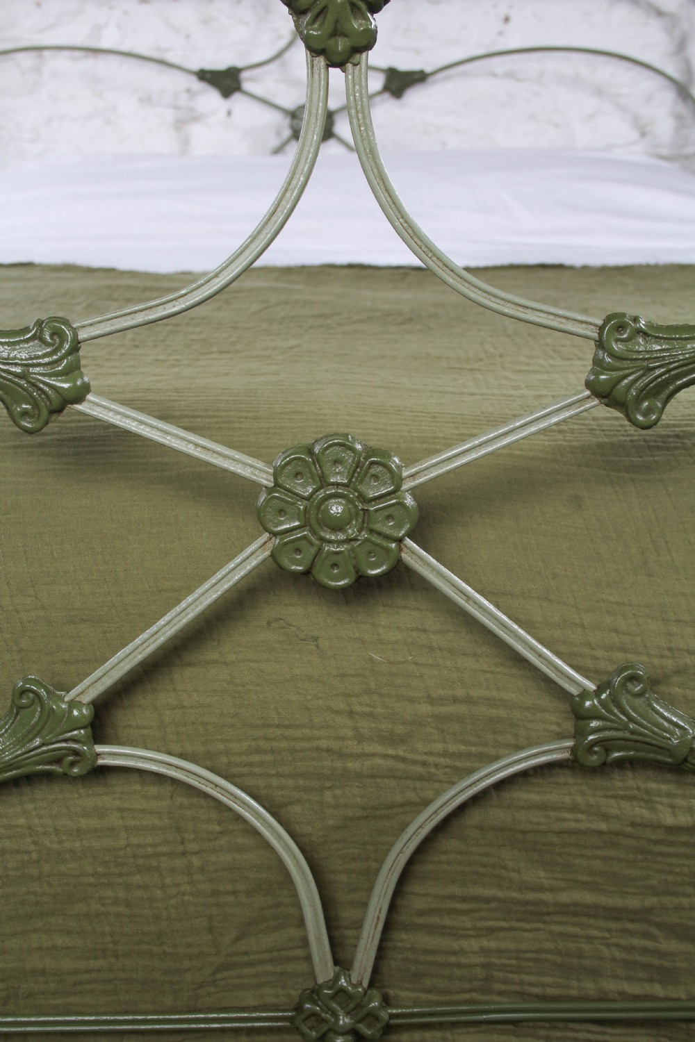 A green painted cast iron king-size bedstead featuring decorative central rosette castings, curved top rails, and metal strapwork. View V