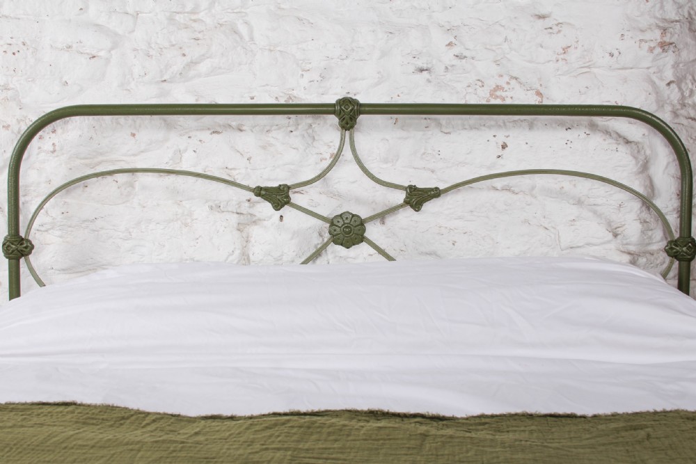 A green painted cast iron king-size bedstead featuring decorative central rosette castings, curved top rails, and metal strapwork. View VI