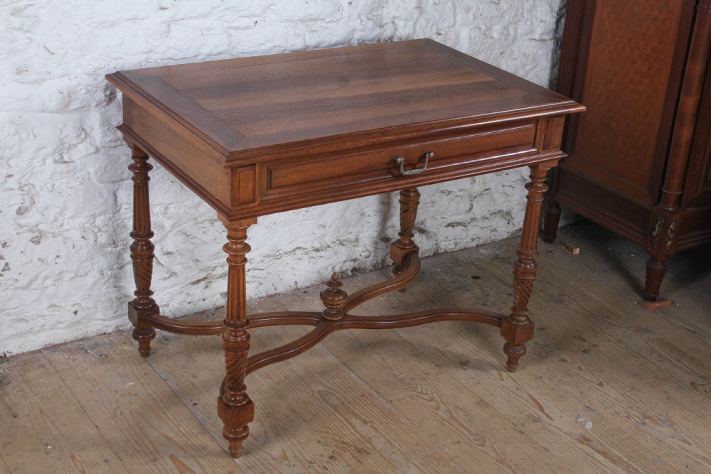 A Louis XVI style fruitwood table featuring a single frieze drawer with brass handle, turned fluted legs, and an X-frame stretcher with a central finial.