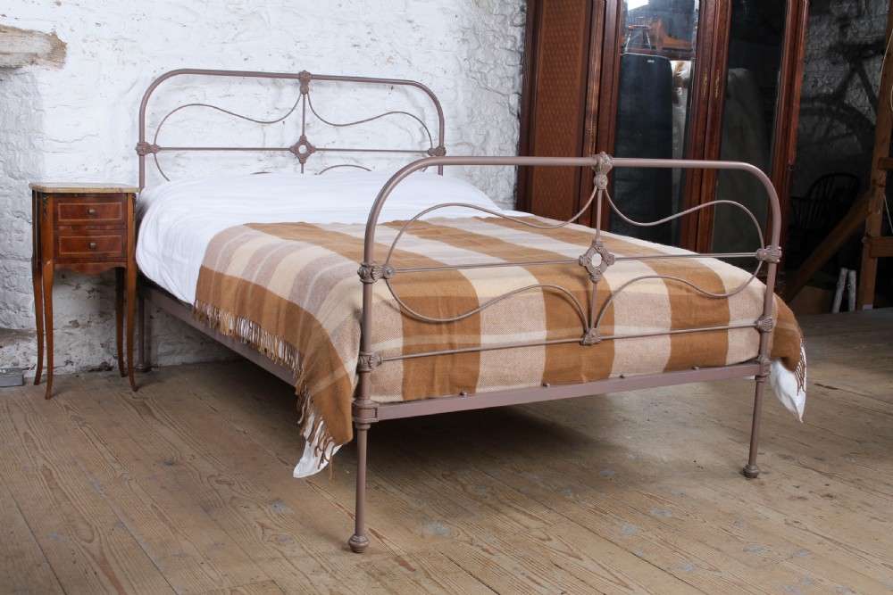 An antique Irish double bed frame constructed from painted iron with curved metal scrollwork and decorative cast medallions.