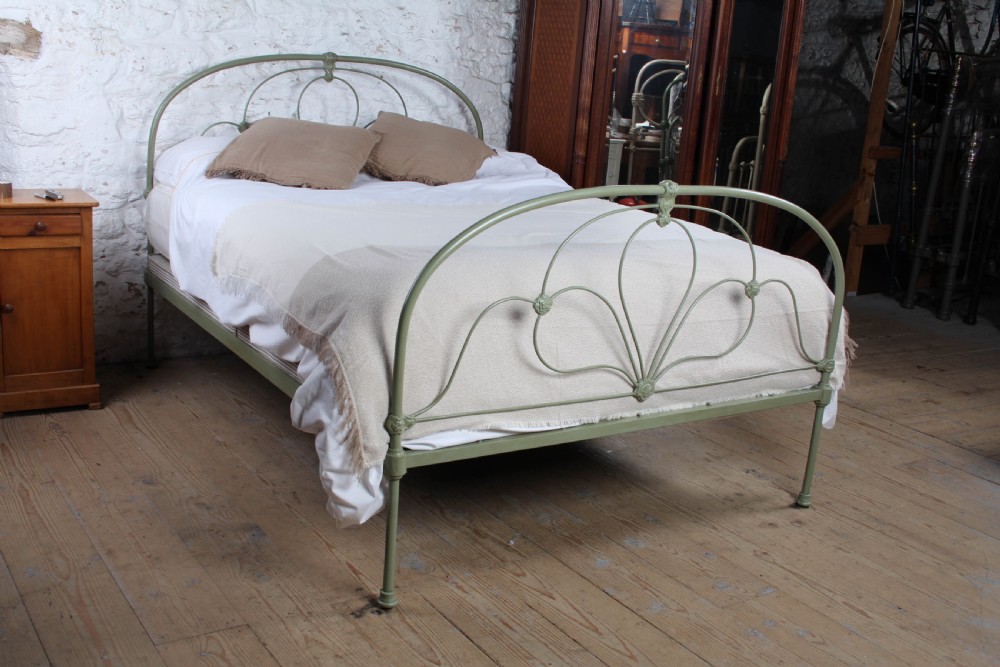 A green painted iron bedstead featuring arched headboard and footboard frames with decorative looped ironwork and cast medallions.