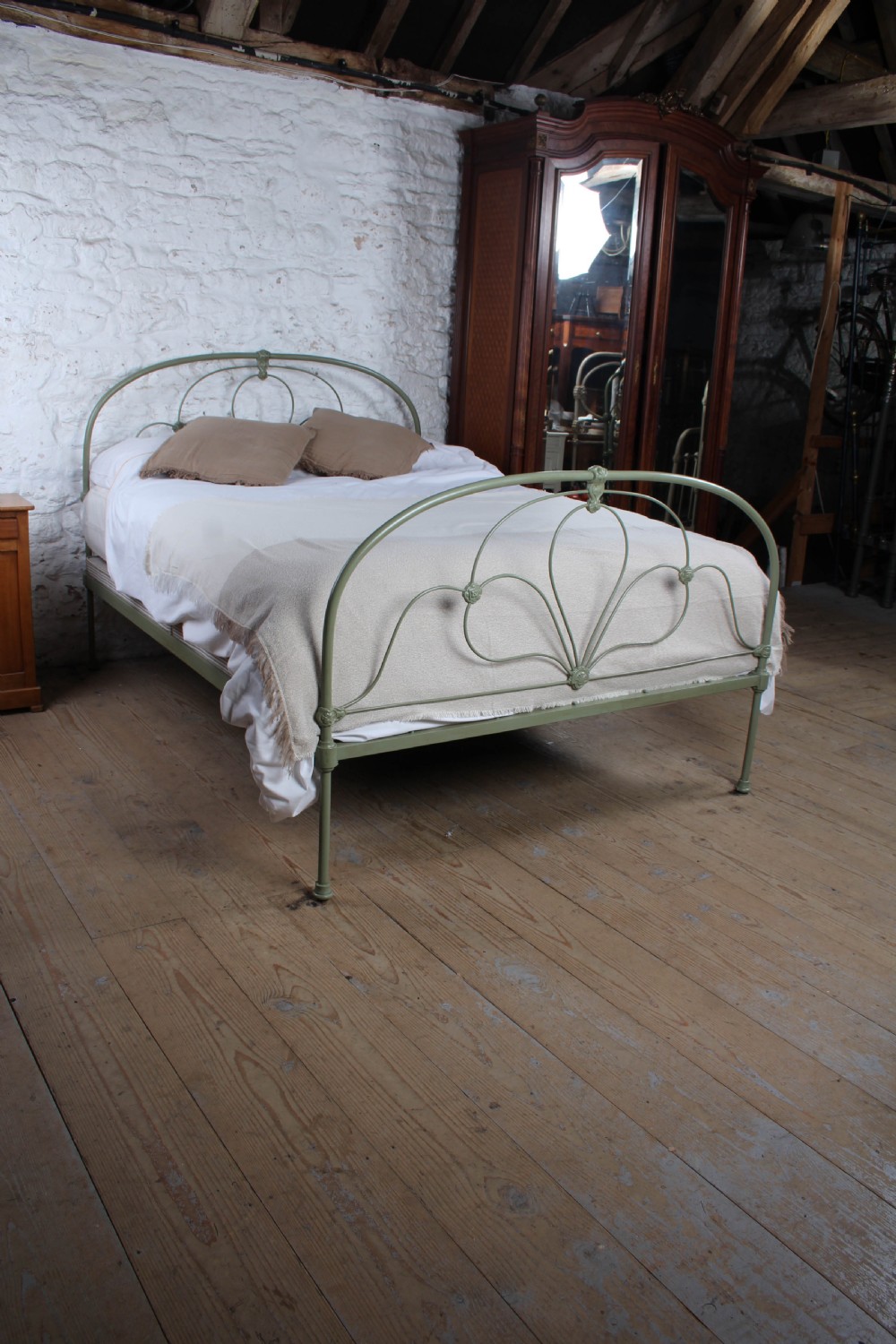 A green painted iron bedstead featuring arched headboard and footboard frames with decorative looped ironwork and cast medallions. View II